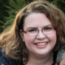 Woman with glasses smiling outdoors with greenery in the background
